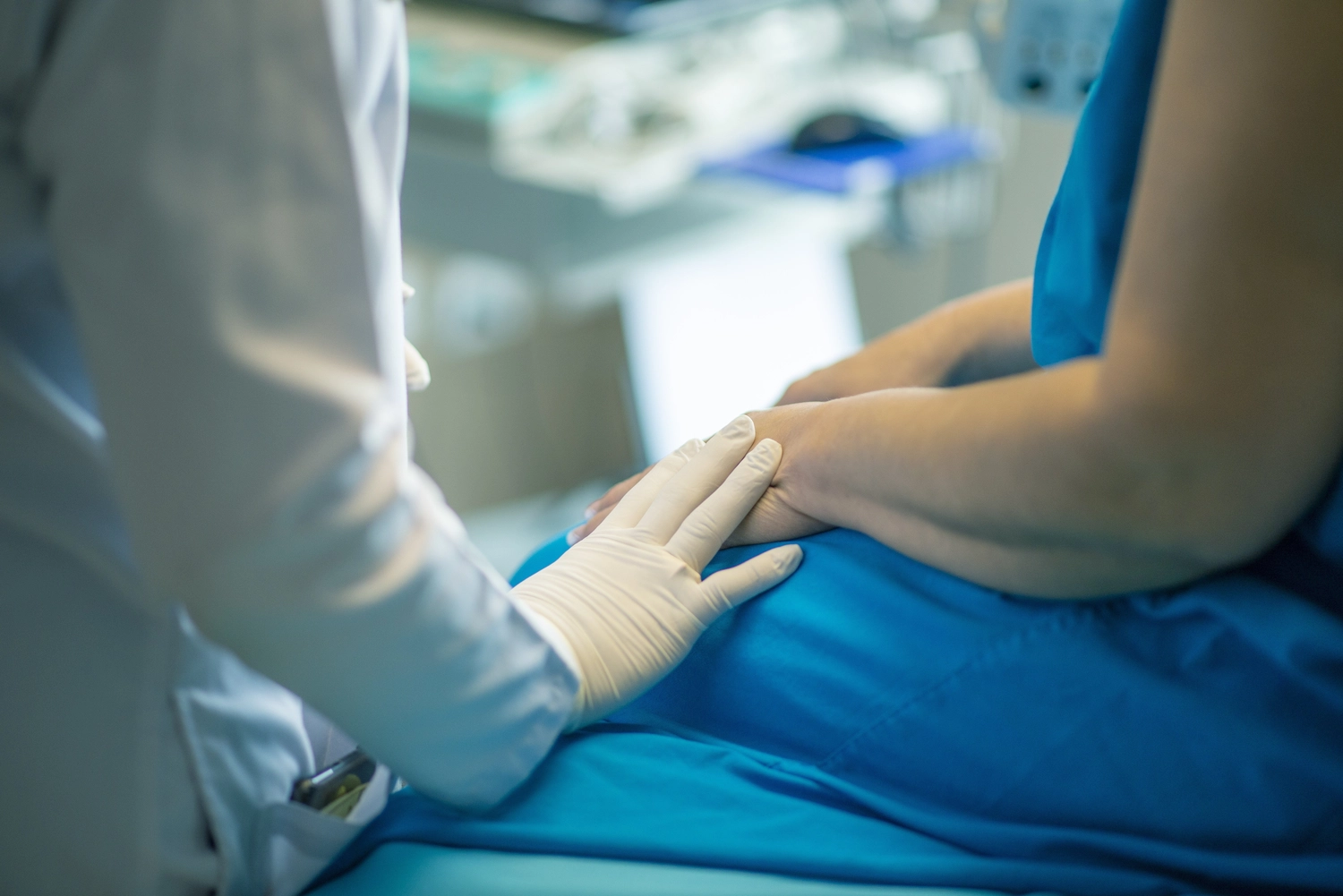 Pflegedienst Döring - Ambulanten Pflegedienstes - Eine über die Schulter aufgenommene Aufnahme zeigt eine medizinische Fachkraft in weißem Kittel und Handschuhen, die tröstend die Hand auf die Hand eines Patienten in einem blauen Kittel legt.