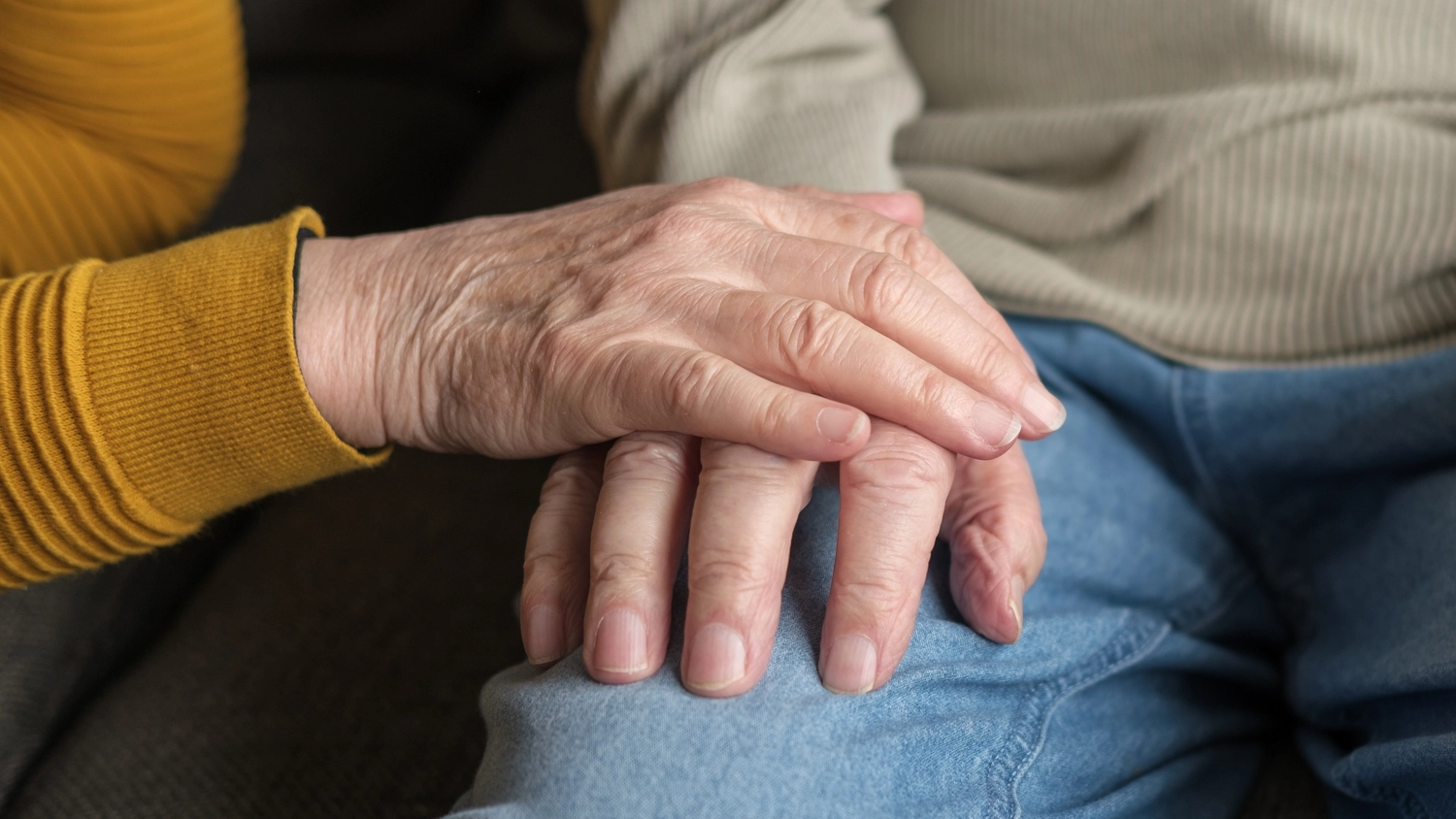Pflegedienst Döring - Ambulanten Pflegedienstes - Die Hand einer älteren Person ruht sanft auf der Hand einer anderen Person, die auf einem mit blauen Jeans bekleideten Schoß ruht.